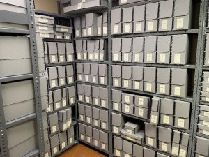Archival document boxes on steel shelves in the storage room at the back of the classroom.